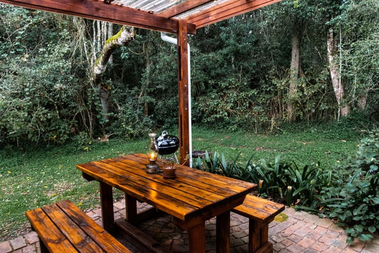 The private back porch with wooden table, bench set and weber at The Bush Pig Cottage along the forest edge