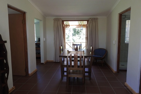 The main living area with wooden dinging room table leading to the back deck at The Bush Buck Cottage